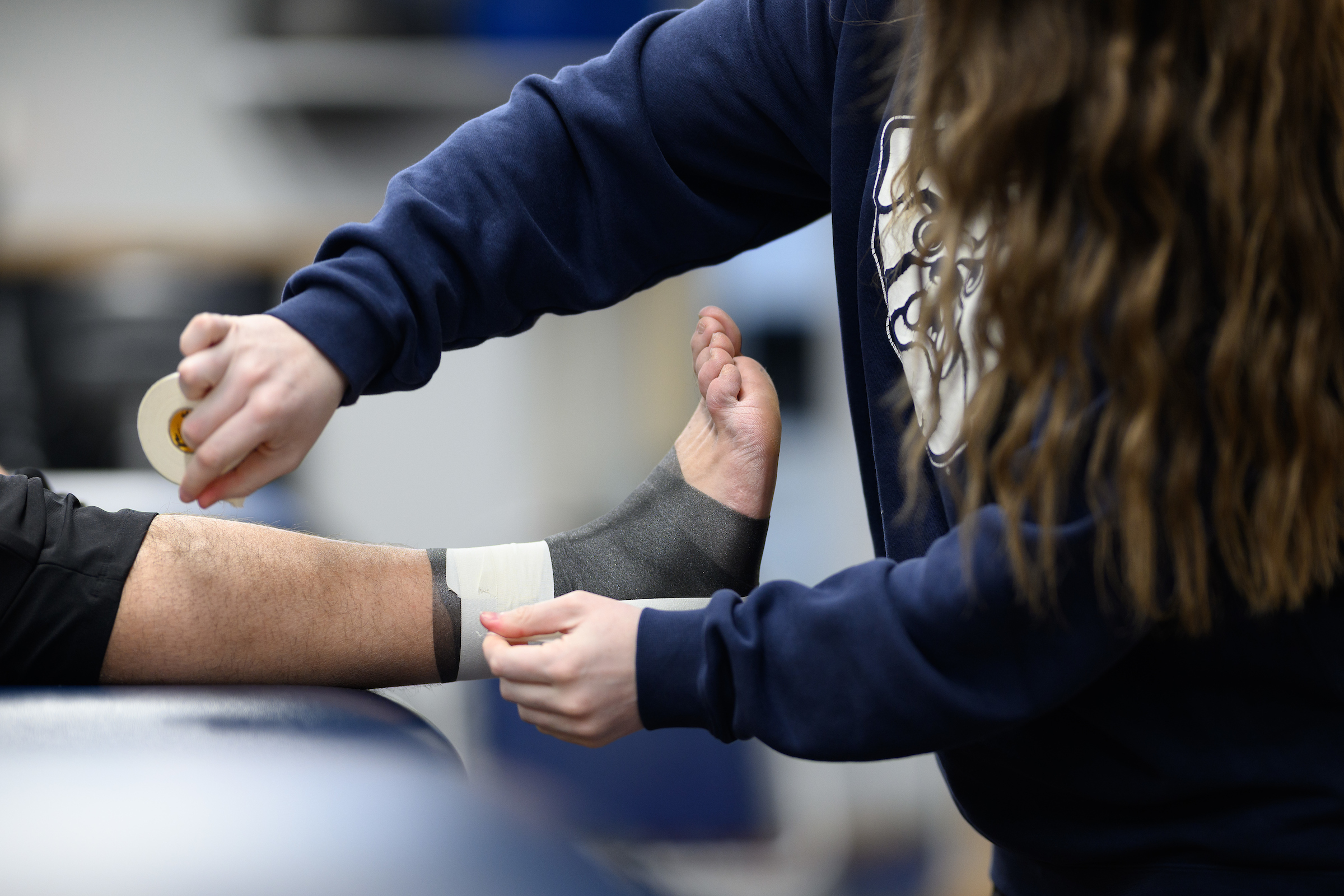 A student athletic trainer wraps an athlete's ankle.